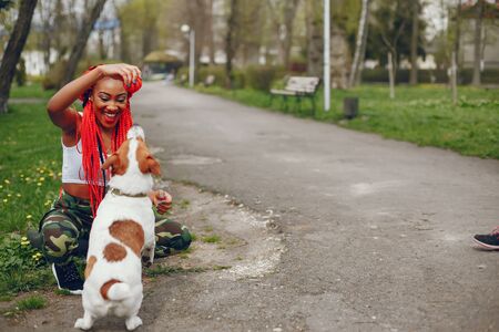 A young and stylish dark-skinned girl with red dreads walking in the summer park with dogの写真素材