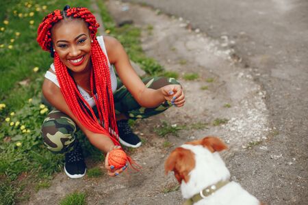 A young and stylish dark-skinned girl with red dreads walking in the summer park with dogの写真素材