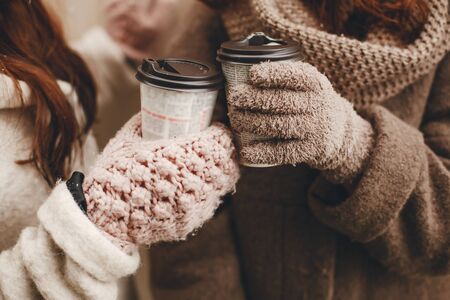 two bright and merry girls standing near wood wall and drinking coffeeの写真素材