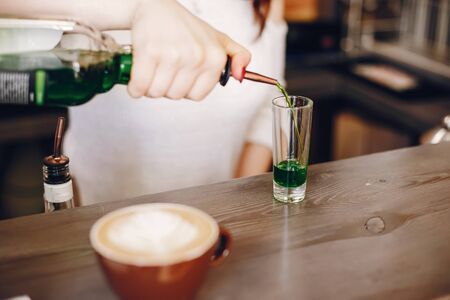 Woman in a white sweater pouring green syrop into glassの写真素材