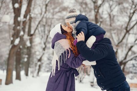 Family have fun in a winter park. Stylish mother in a purple jacket. Little girl in a winter...