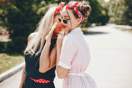 Stylish girls in a retro dress. Vintage ladies in a summer park. Two women have funの写真素材