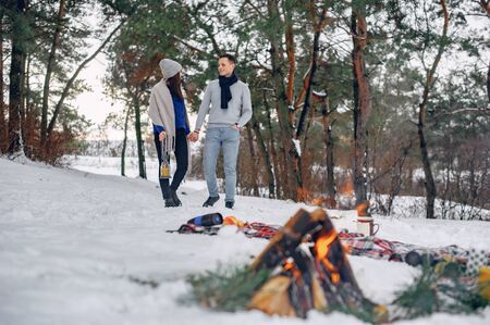 Couple in a winter forest. Beautiful girl in a blue sweater. Boy and girl near bonfire