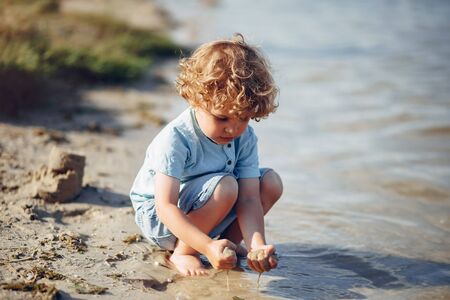 Beautiful little boy in a blue shirt. Childred playing in a summer beach. On a sandの写真素材
