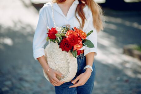 Beautiful girl in a white blouse. Woman in a summer city. Lady with bouquet of flowersの写真素材