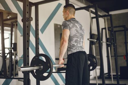 Sports man in the gym. A man performs exercises. Guy in a gray t-shirt