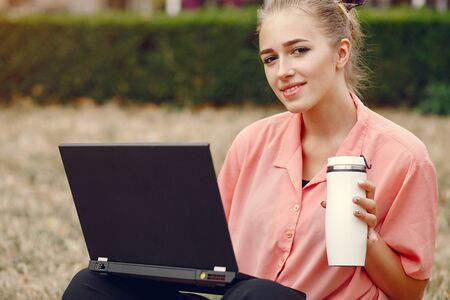 Girl in a pink shirt sitting in a parke and use the laptop