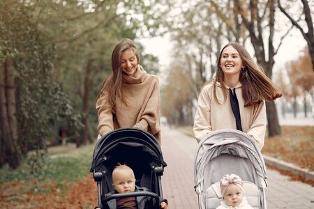 Two young mothers walking in a autumn park with carriages