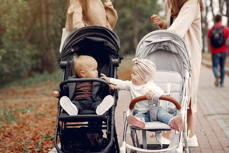 Two young mothers walking in a autumn park with carriages