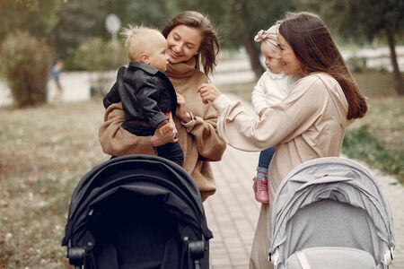 Two young mothers walking in a autumn park with carriages