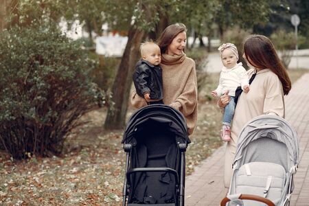 Two young mothers walking in a autumn park with carriages