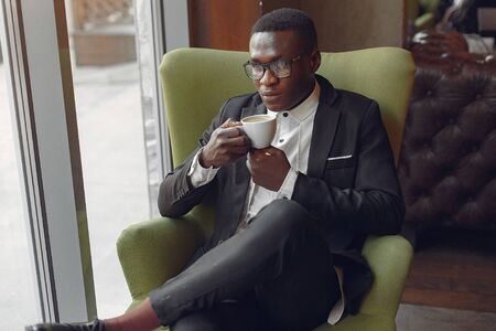 Black man sitting in a cafe and drinking a coffeeの写真素材