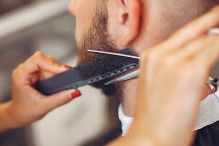 Man with a beard. Hairdresser with a client. Woman with scissors and a combの写真素材