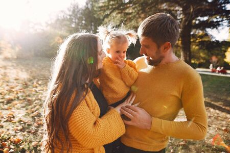 Family in a autumn park. Woman in a yellow sweater. Cute little girl with parentsの写真素材