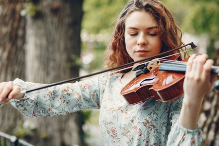 Beautiful girl in a summer park with a violinの写真素材