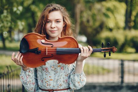 Beautiful girl in a summer park with a violinの写真素材