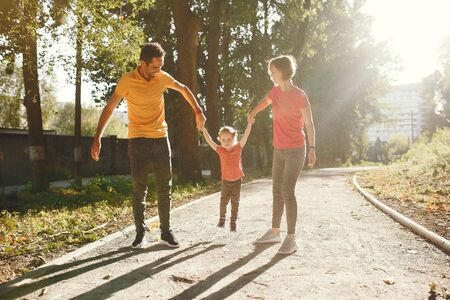 Family with cute little daughter. Father in a yellow t-shirt. People walks in a park.の写真素材