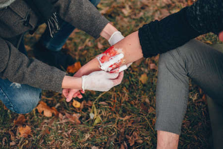 Providing first aid in the park. Man bandaged injured arm. Guy helps a friend.の写真素材