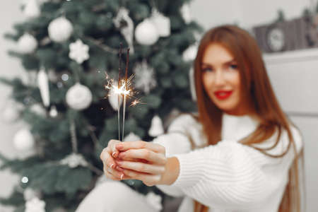 Woman in a white sweater sitting by the christmass treeの写真素材