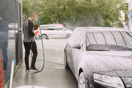 Man in a black sweater. Male washing a car. Guy spray a water.の写真素材