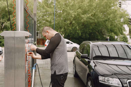 Handsomen man in a black sweater washing his car