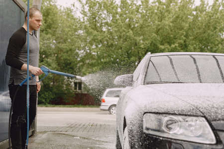Handsomen man in a black sweater washing his carの写真素材