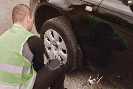 Worker changes a broken wheel of a car. The driver should replace the old wheel with a spare. Man changing wheel after a car breakdown.の写真素材