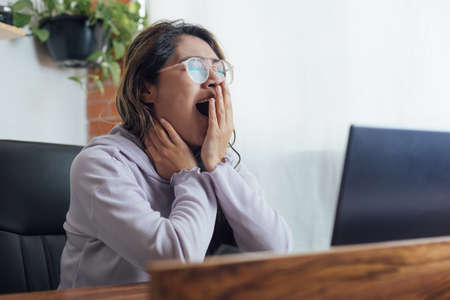 Mexican woman with home office is bored and sleepy in front of the computerの写真素材