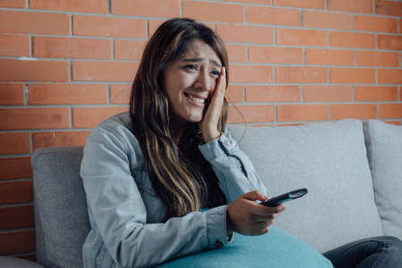 Mexican woman points with the control of the television excited and happy. home entertainment
