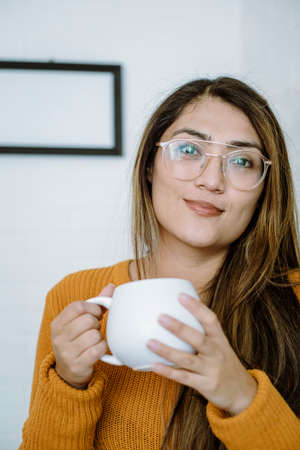 Mexican young woman drinks from a white cup with natural poseの写真素材