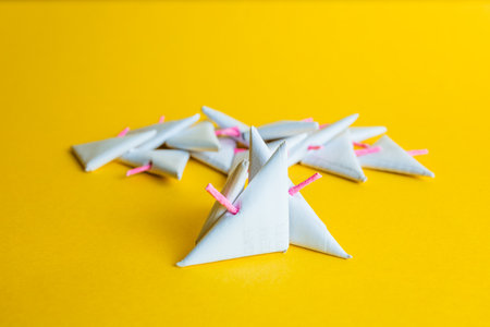 Close-up of a pile of white paper triangular-shaped objects, scattered and with pink fuses, on a...
