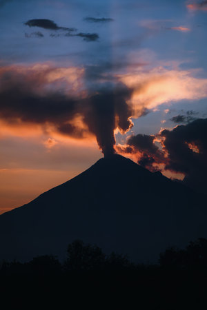 Powerful silhouette of Mexico's Popocatepetl Volcano during an ash exhalation, with a dramatic sky...