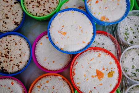Close-up of fresh, round, artisanal cheeses with chili and peppers, displayed in vibrant plastic colored baskets.の写真素材