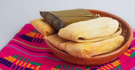 Close up of tamales wrapped in corn and banana leaves on clay plate, highlighting textures of traditional Mexican soul foodの写真素材