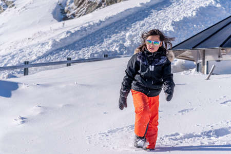 Child walking in snow. One Asian girl in ski-wear, sunglasses and gloves playing in winter. Happy childhood.の写真素材