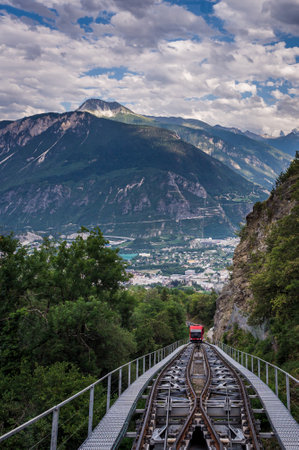 Crans Montana, Valais Canton, Switzerland - 15 July 2023: One red Swiss funicular from Sierre to Crans Montana. Public transport cable railway with scenic view over the city and mountain.のeditorial素材