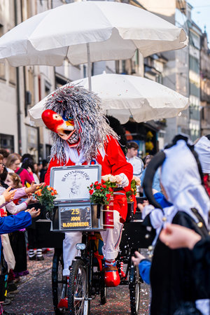 Basel, Switzerland - March 25, 2026: Traditional masked carnival characters riding decorated bicycle carts and interacting with the crowd during the Basel Fasnacht parade, the most famous carnival festival in Switzerland.のeditorial素材