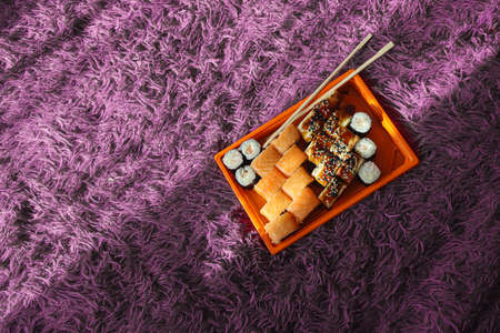 Set of different types of sushi rolls with shrimp, salmon, eel, in an orange box on a purple fluffy carpet or bedspread. Japanese Food Delivery Conceptの写真素材