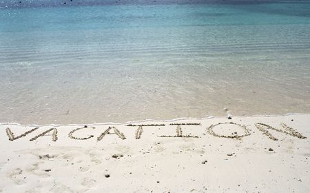 Vacation written in the sand of a tropical beach shoreline.