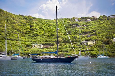 Large and luxurious sailboats anchored infront of beautiful tropical island.