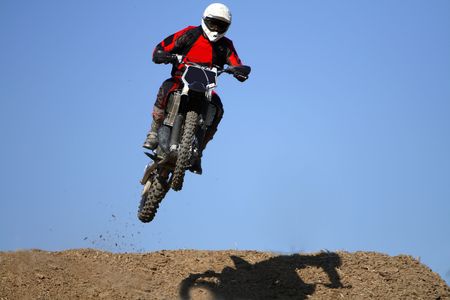 Man jumping high in a motocross bike across a slope on a desert.の写真素材
