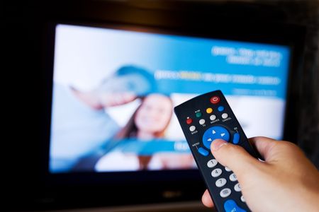 Hand pointing a tv remote control towards the television.