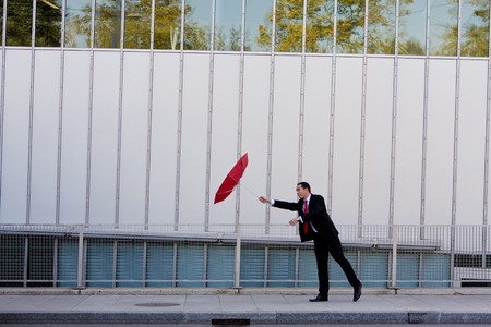 Asian business man holding on to his umbrella on a windy dayの写真素材