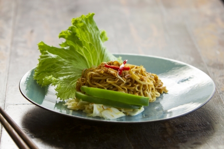 Chinese style fried yellow noodles served on a blue plate with a leaf of saladの写真素材