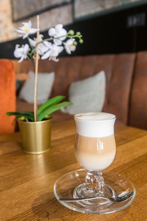 A tall glass of cappucinno or cafe latte served on a saucer with a thick white foamの写真素材
