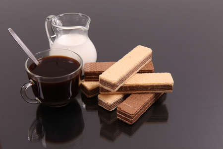 Coffee with milk and wafers against a dark background with reflexionの写真素材
