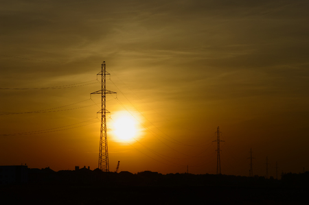 Outlines of masts of high voltage power lines in sunset lightの写真素材