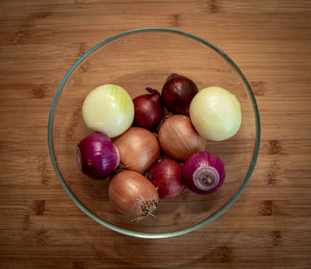 some peeled and unpeeled red and yellow onions in a bowl on a wooden tableの写真素材