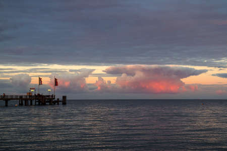 a jetty in front of beautiful colored clouds by the seaの写真素材