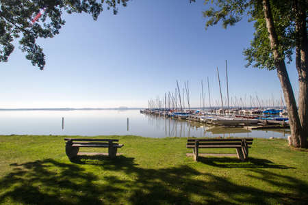 two park benches on a green meadow in front of a jetty in summerの写真素材